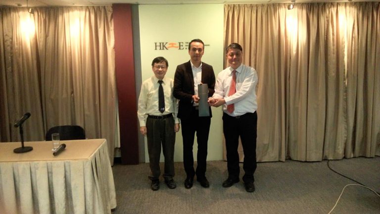 Three men in business attire posing for a photo at an event, one holding a trophy.