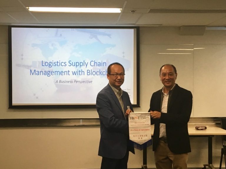 Two men in a presentation room exchanging a token of appreciation for logistics supply chain management with blockchain.