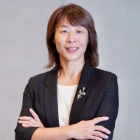 Professional woman with short brown hair, wearing black blazer over white top, arms crossed, smiling.