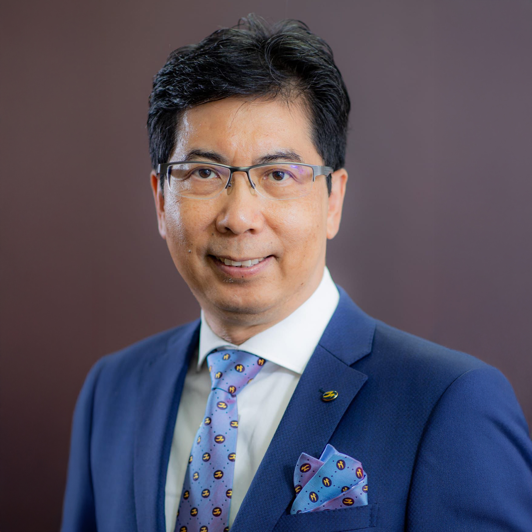 Portrait of Ir Prof Simon Cheung wearing glasses, blue suit, and patterned tie.