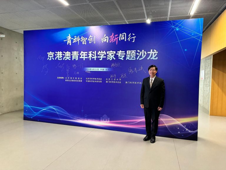 Man in suit standing before event backdrop for Beijing-Hong Kong-Macao Youth Scientists Forum, September 21, 2024.