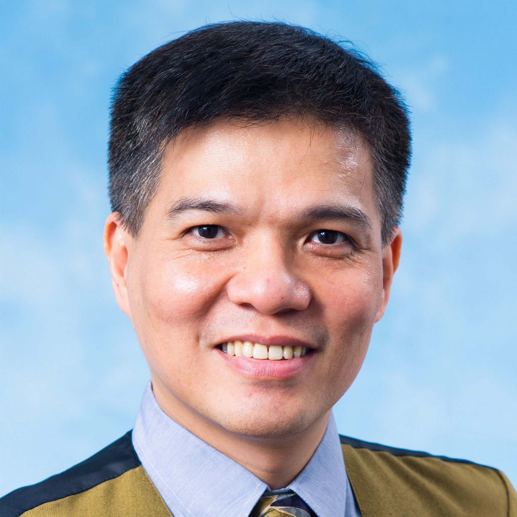 Portrait of Jonathan Chairman, smiling, wearing a collared shirt and tie against a blue background.