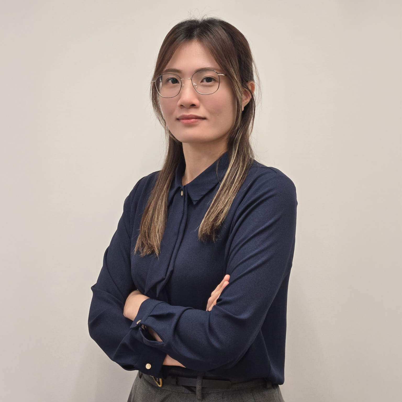Yumi CHU Yuet Ming, wearing glasses and a navy shirt, arms crossed, neutral expression