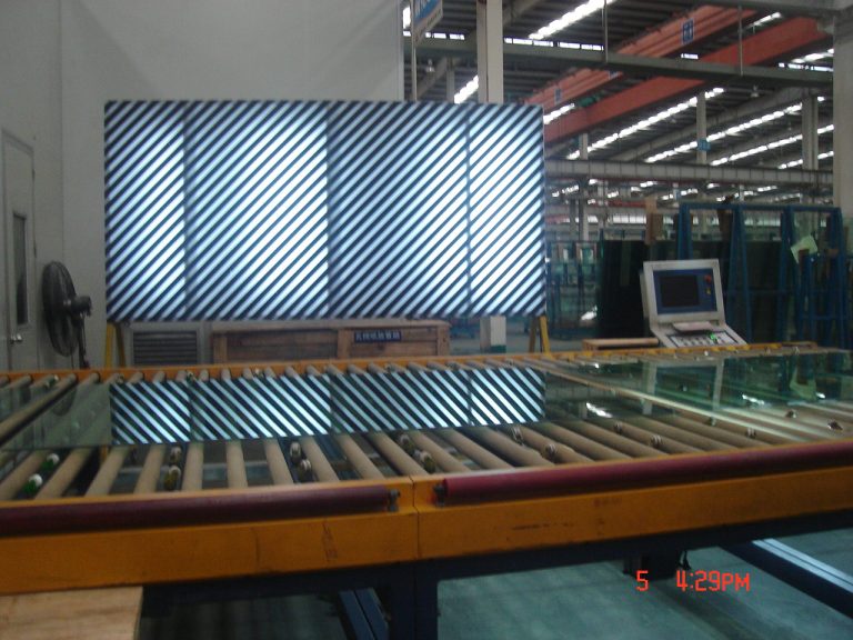 Factory conveyor system transporting glass panels under striped lighting.
