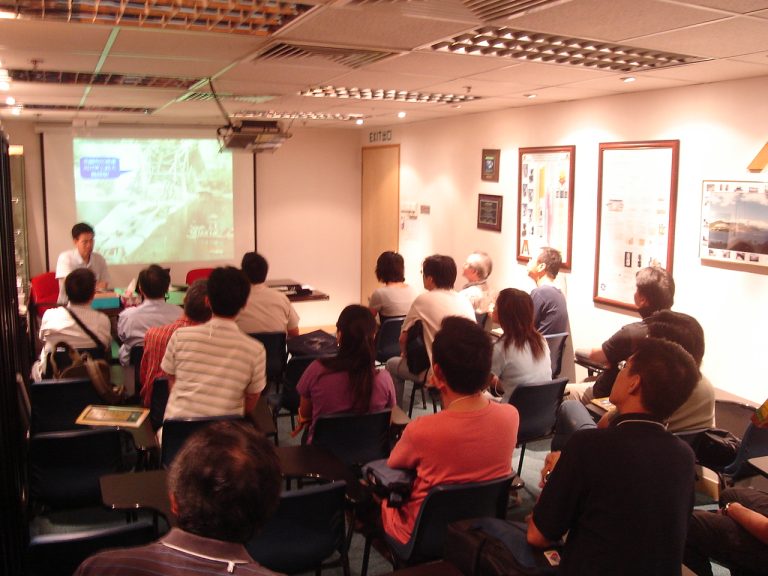 Audience attending presentation in conference room with projector screen displaying content.