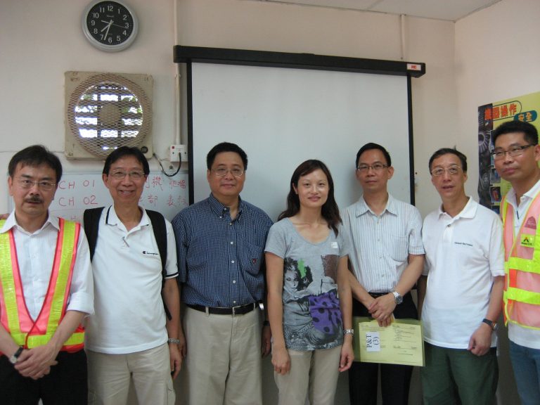 Group of six people posing for photo in classroom setting, one holding certificate.
