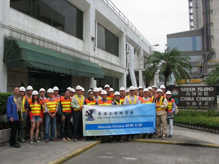 Group of engineers in safety gear holding banner outside China Cement plant.