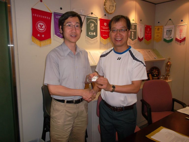 Two men shaking hands in an office, one presenting a watch.