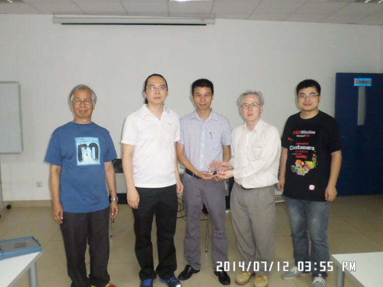 Five men posing indoors, two holding a clear award, date stamp visible.
