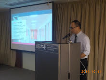 Man speaking at podium during presentation with projected slides behind him