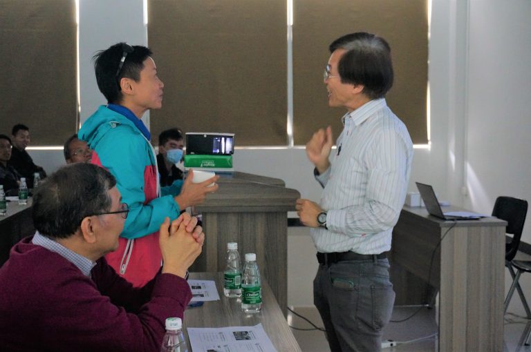 Two people engaged in conversation at a conference table with others seated nearby.