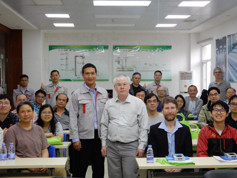 Group of people in a classroom setting with PVB resin production process charts on the wall.