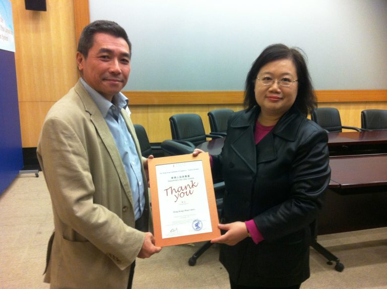 "Man and woman holding framed ""Thank You"" certificate in conference room."