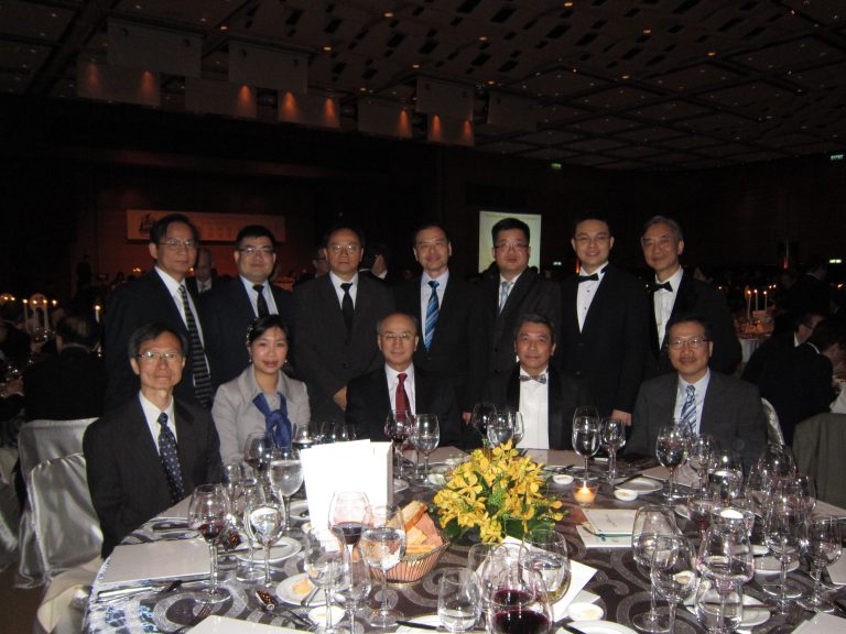 Group photo of attendees at formal dinner event, seated and standing around decorated table.