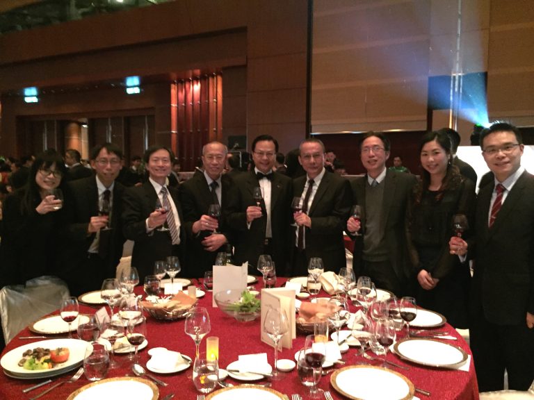 Group of professionals posing with wine glasses at a formal dinner event.