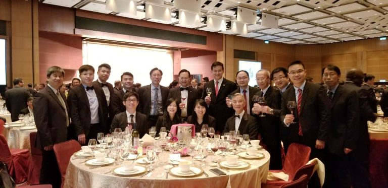 Group photo of attendees at HKIE Annual Dinner, posing with wine glasses at a formal banquet table.