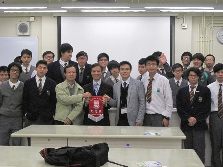 Group of students and adults in formal attire posing with a red commemorative banner in a classroom.