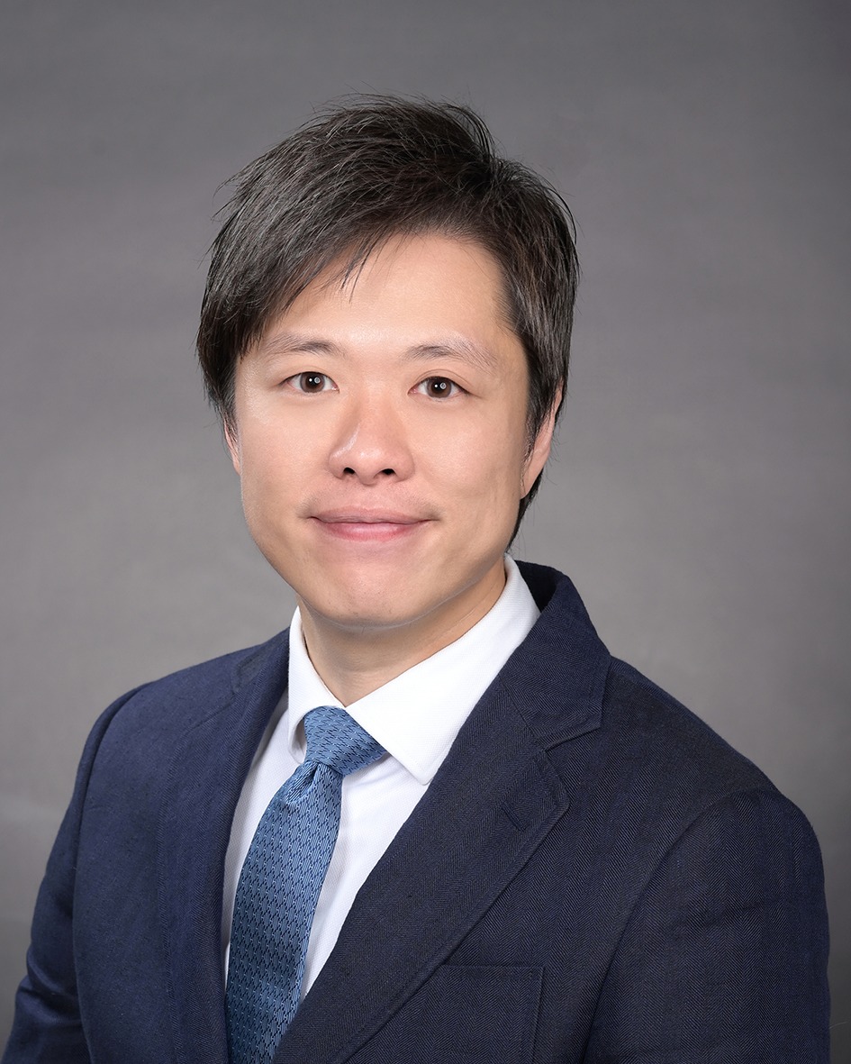 Portrait of a man in a dark suit and blue patterned tie against a gray background.