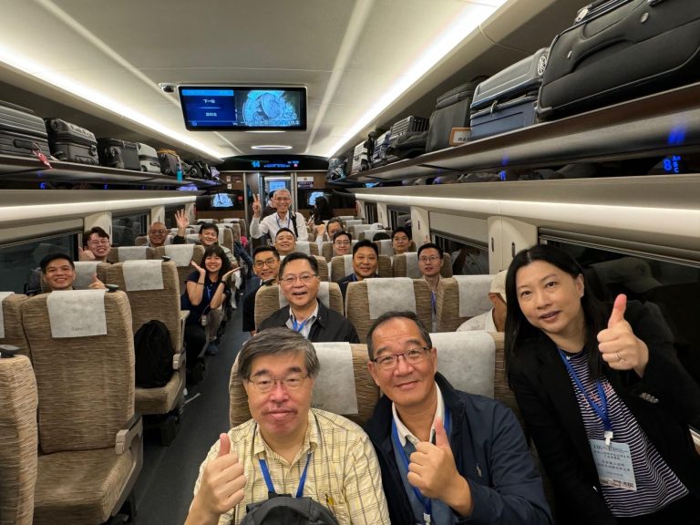 Group of travelers posing with thumbs up inside a modern train carriage, luggage overhead.