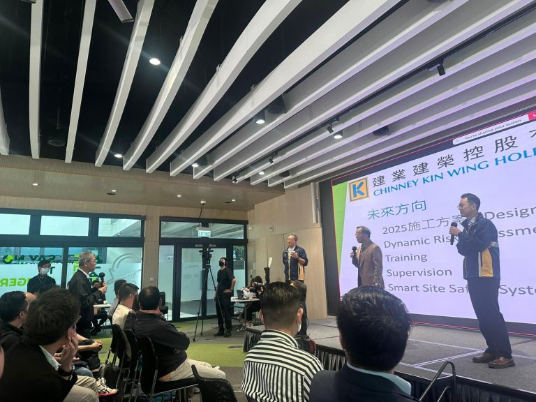 Three men presenting at a corporate event with audience seated, large screen displaying company name and future direction topics.