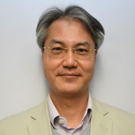 Portrait of a man with glasses and gray hair wearing a light jacket.