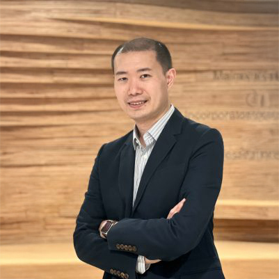 Man in dark suit smiling with arms crossed against wooden background