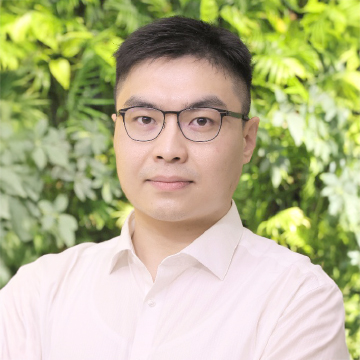 Man with glasses and light-colored shirt against green foliage background