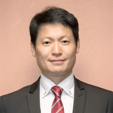 Professional headshot of a man in suit and red tie against pink background