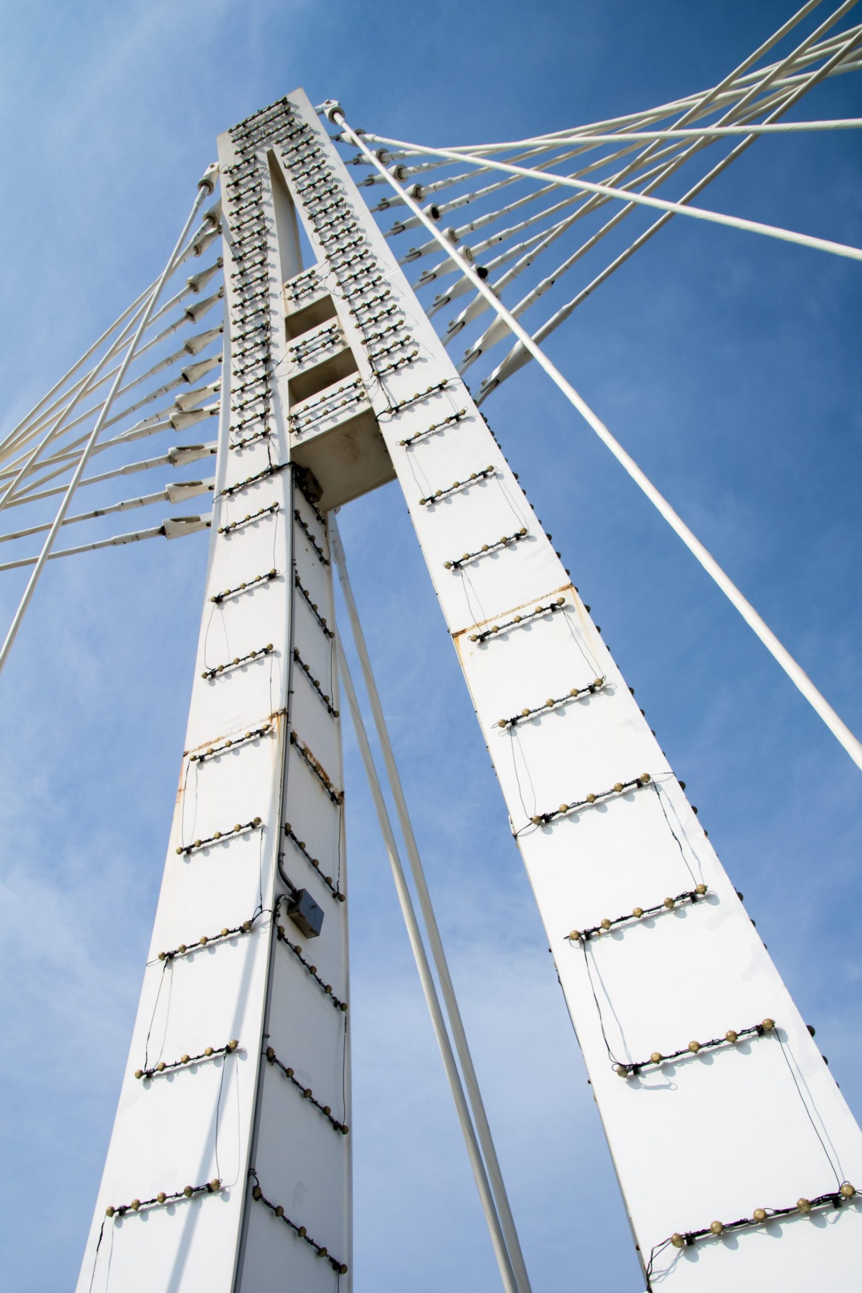 Low-angle view of white suspension bridge towers against blue sky with cables