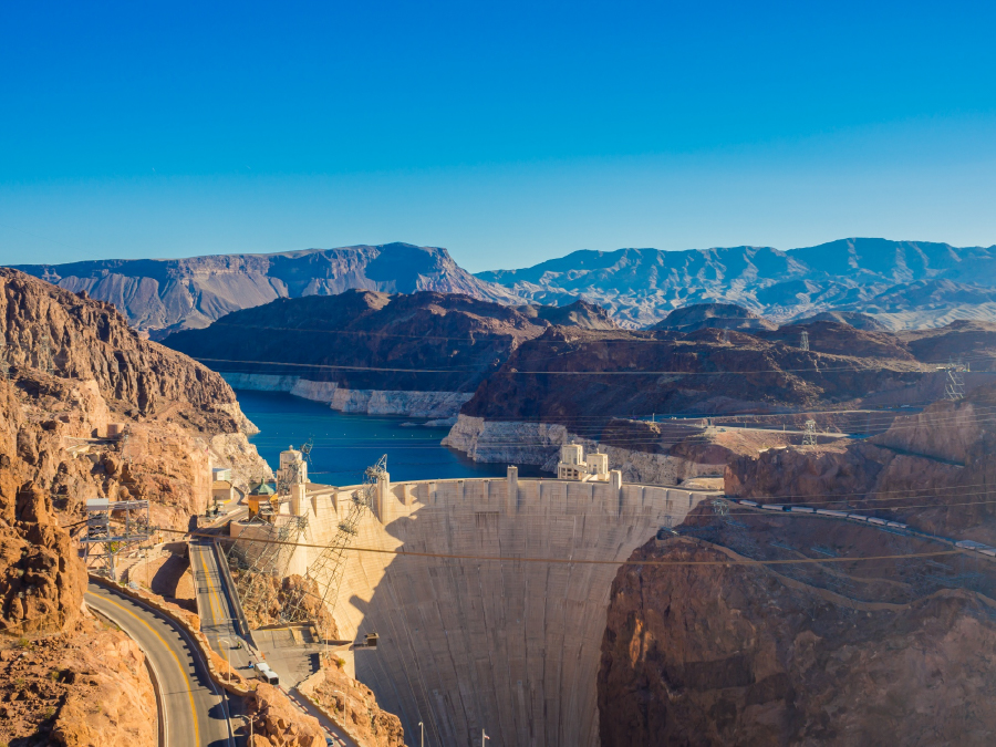 Hoover Dam spanning canyon with reservoir, mountains, and road under clear blue sky