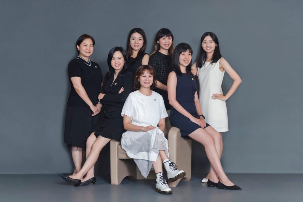 Six women posing for a group photo, three standing, three seated on a bench.