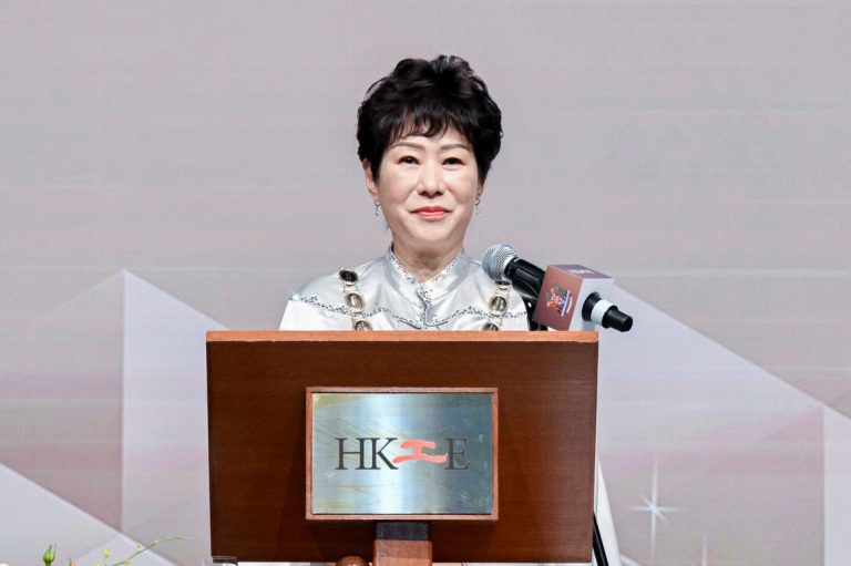 Woman speaking at podium with HKIE logo, wearing formal attire and earrings.