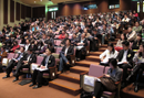 Audience seated in tiered rows at a conference or lecture hall.