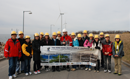 Group of people in hard hats posing with a large model of a wind turbine.