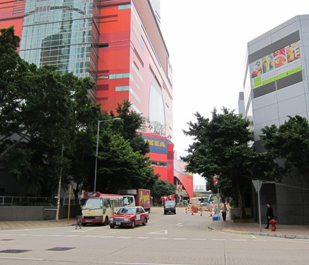 Urban street scene with modern buildings, trees, and vehicles.