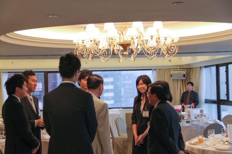 Business professionals networking in a formal dining room under a chandelier.