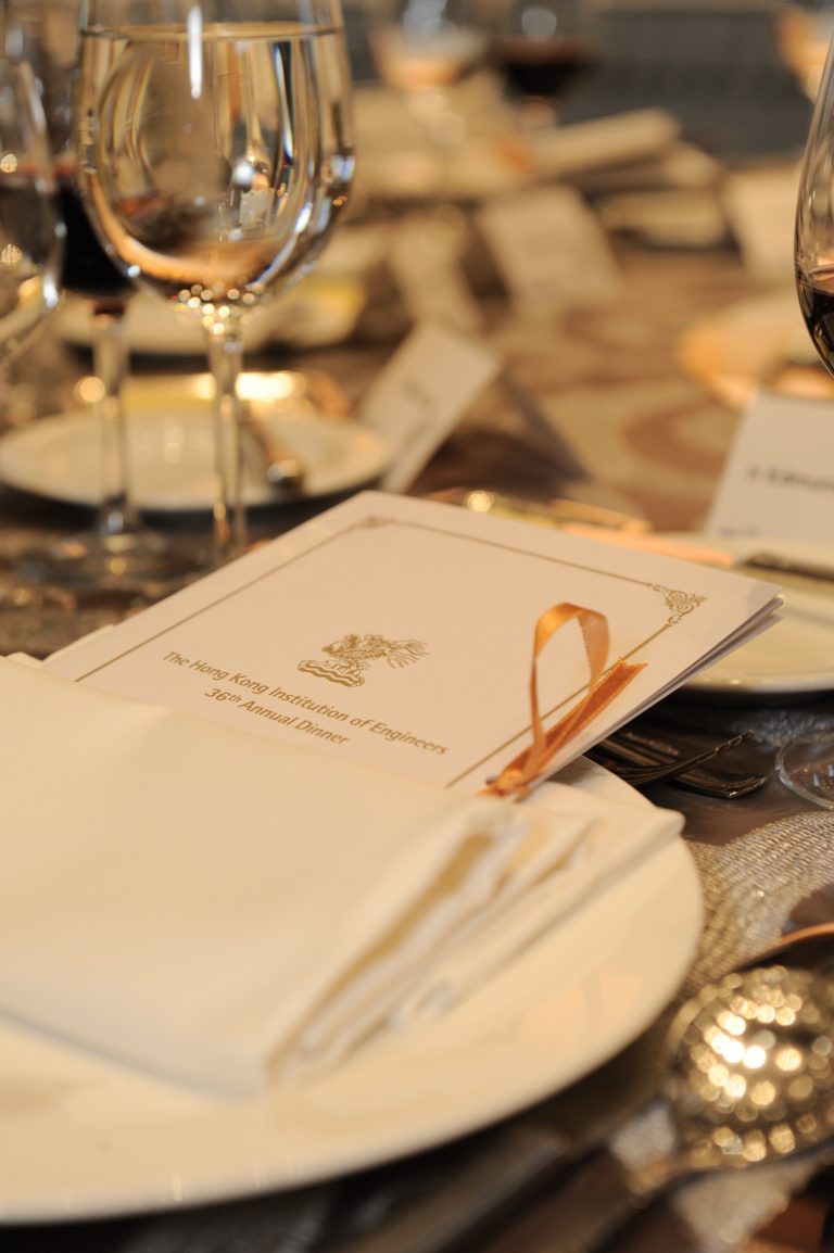 Menu for The Hong Kong Institution of Engineers 36th Annual Dinner, tied with gold ribbon, on elegantly set table.