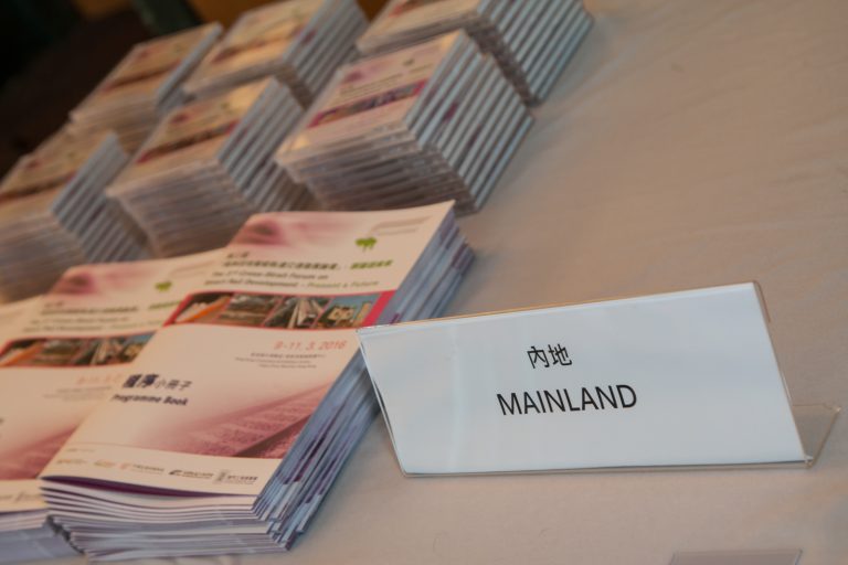 "Stacked programme books with a ""MAINLAND"" sign in front."