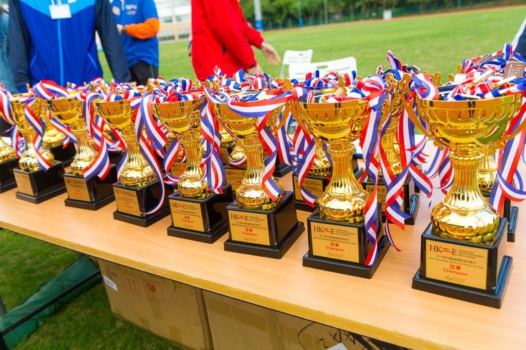 Row of gold trophies with red, white, and blue ribbons on a table.