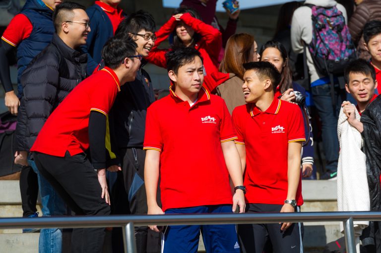 Group of young people in red polo shirts laughing and socializing outdoors.