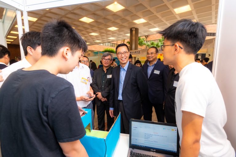 Group of people interacting at a tech exhibition booth with a laptop and prototype.