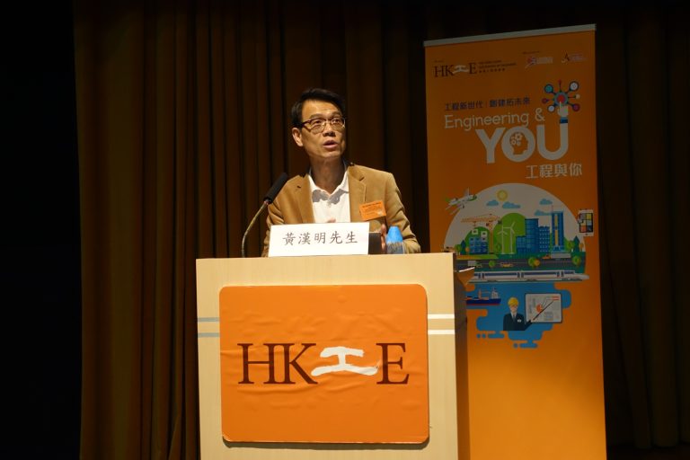 Man speaking at podium with HKIE logo, behind banner promoting engineering.