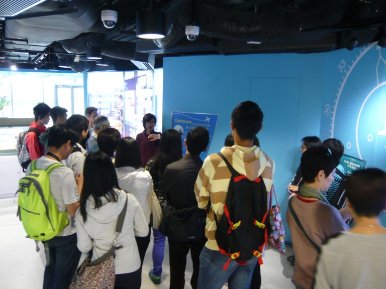 Group of visitors listening to guide at aviation exhibition booth