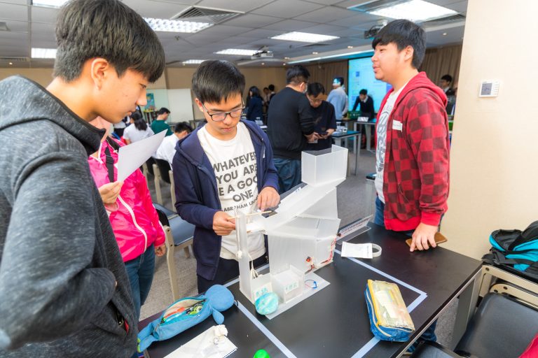 Students examining a transparent architectural model at a design exhibition.