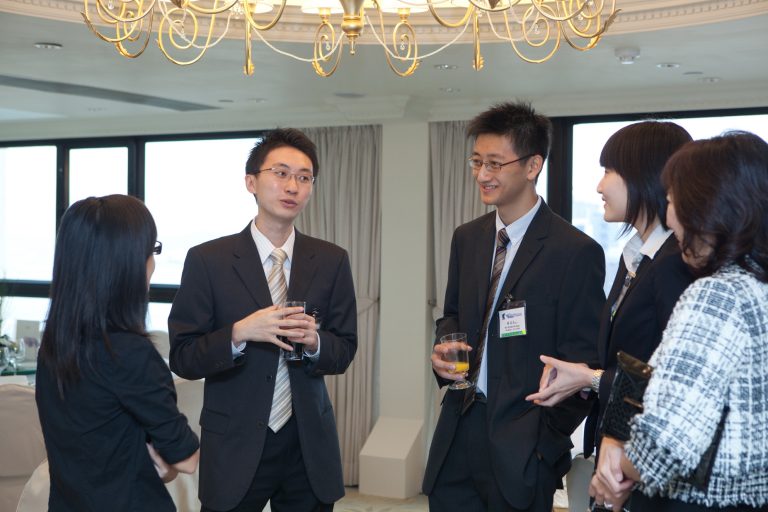 Business professionals conversing at a formal event under a chandelier.