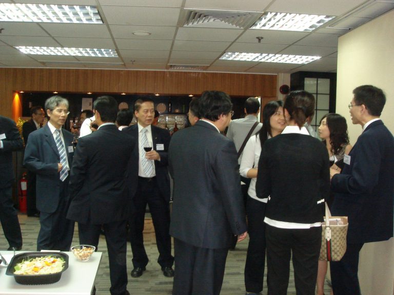Professionals networking at a business event, holding drinks and conversing in a conference room.