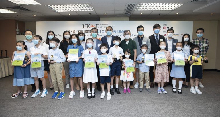 Children and adults wearing masks pose with awards and certificates at an engineering competition event.