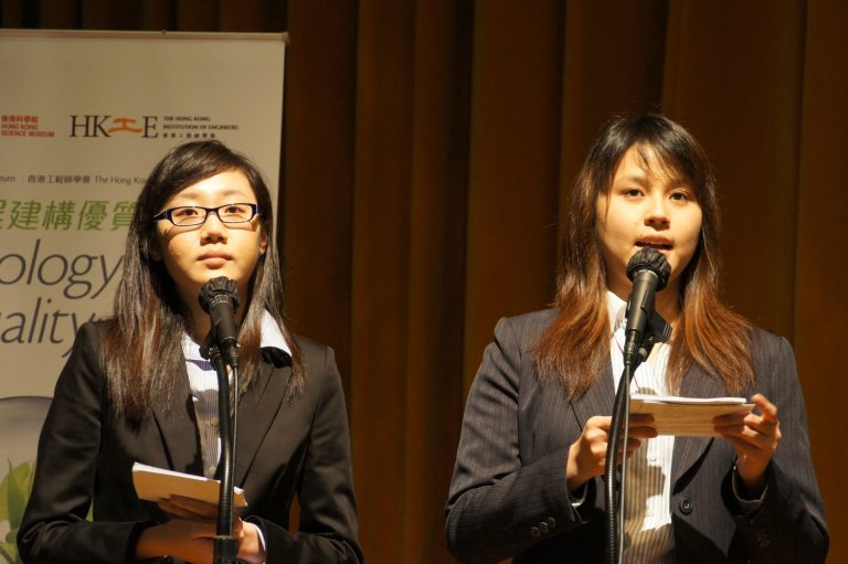 Two women in business attire speaking at microphones during an event.