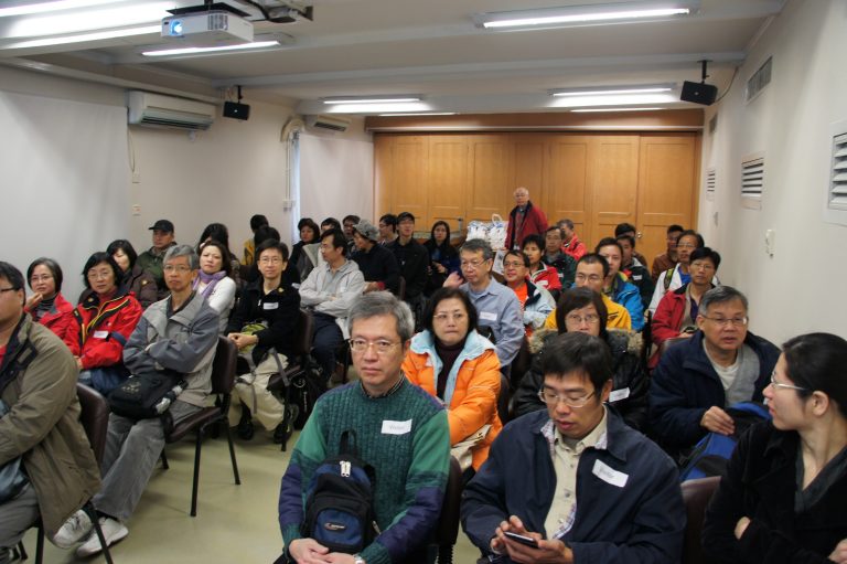 Audience seated in a room, attentively listening to a presentation.