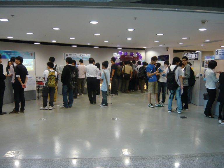 Students queueing at university event booths with balloons and banners.